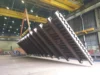 A large metal structure being lifted by a crane inside an industrial workshop.