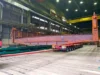 A large steel beam being transported on a specialized trailer inside an industrial warehouse.