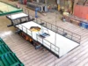 A large metal platform with safety railings, mounted on a vehicle inside an industrial warehouse, with various equipment and tools in the background.