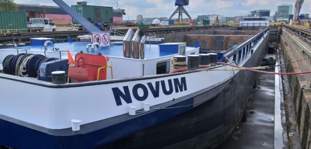 The barge 'Novum' docked in a shipyard for maintenance.