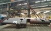 Large metal structure being lifted by cranes in an industrial facility.