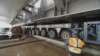 A worker supervises the transport of a large steel structure using a specialized heavy-duty transporter at a construction site.
