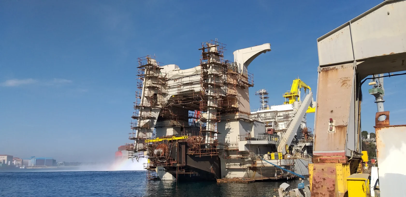 Partially constructed offshore platform at a shipyard with scaffolding and cranes.