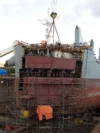 Workers in a dry dock installing a new section onto the rear of the ship.
