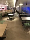 A cozy dining area with wooden tables and a mix of green and black chairs, featuring soft lighting, tiled columns, and a jukebox in the background.