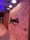 Entrance to restaurant with a brick wall featuring the restaurant's illuminated sign and decorative lighting above.