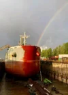 The cargo ship in dry dock with a fresh coat of paint on the hull, illuminated by sunlight under a rainbow.