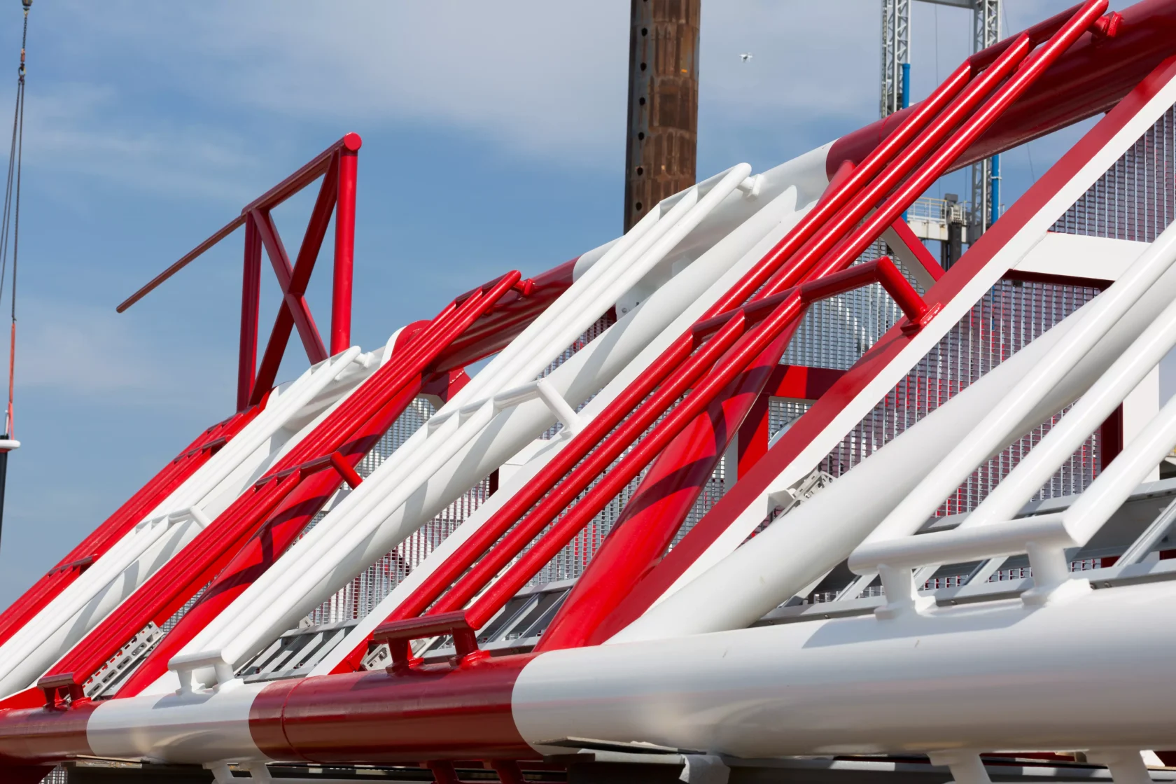 Close-up of a red and white steel lattice structure, likely part of a crane or industrial framework, against a blue sky background.