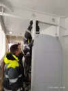 Two workers installing a vertical pipe or support structure inside a building.