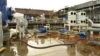 Industrial equipment and piping systems arranged on a wet construction site, with blue protective covers and scattered materials.