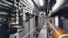 Industrial corridor with pipes and machinery running along the walls and ceiling.