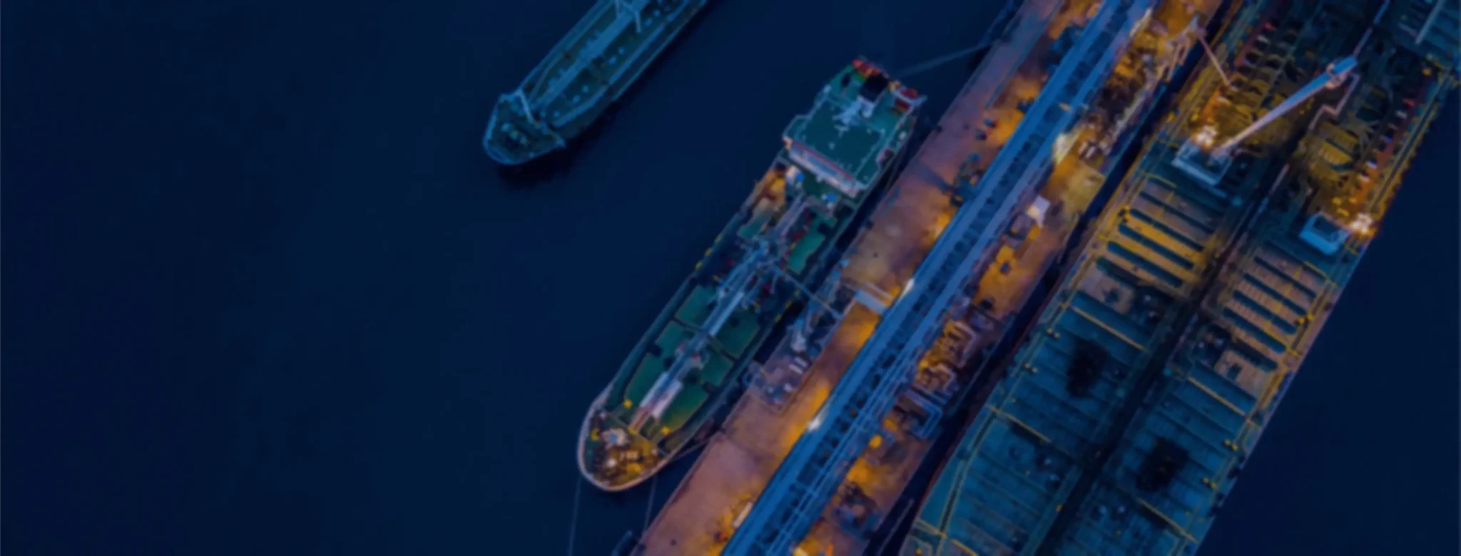 Aerial view of ships docked at a port during nighttime, illuminated by lights.