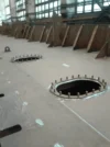 Close-up of a ship's deck under construction, showing two large circular openings and internal bulkheads in a shipyard.