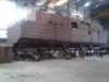 Large ship section under construction, elevated on supports in an industrial shipbuilding facility.