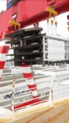 Close-up of a massive red crane lifting a ship's superstructure section at a shipyard during the assembly process.