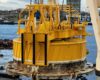 Large yellow industrial structure, part of an offshore equipment, with a waterfront and buildings in the background.