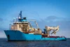 Large blue offshore vessel equipped with cranes and machinery, floating on the water.