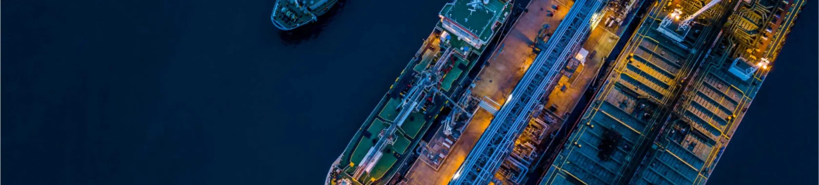 Aerial view of ships docked at a port during nighttime, illuminated by artificial lights.