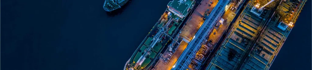 Aerial view of ships docked at a port during nighttime, illuminated by artificial lights.