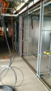 Exposed electrical wiring and conduit framework in an unfinished industrial space, with cables hanging from the ceiling and metal studs ready for wall installation.